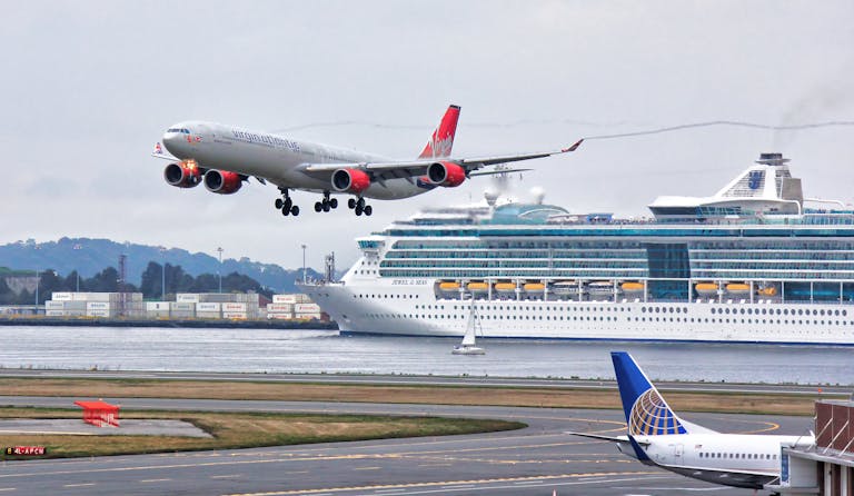 A thrilling view of an airplane landing with a cruise ship passing by in Boston Harbor.