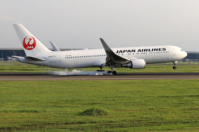 A Japan Airlines aircraft lands on a tarmac with visible landing gear smoke.