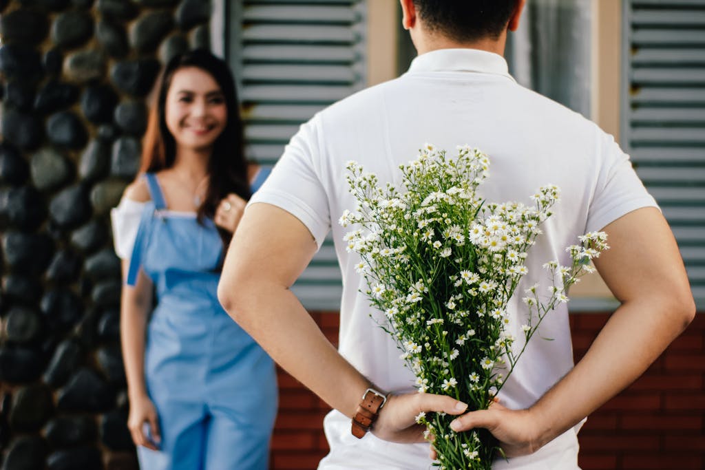 A man surprises his partner with flowers behind his back, symbolizing love and romance.