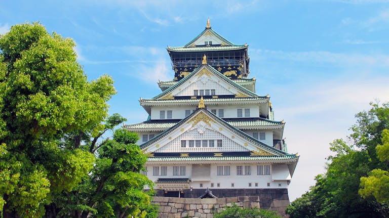 A stunning view of Osaka Castle surrounded by vibrant greenery under a clear blue sky.