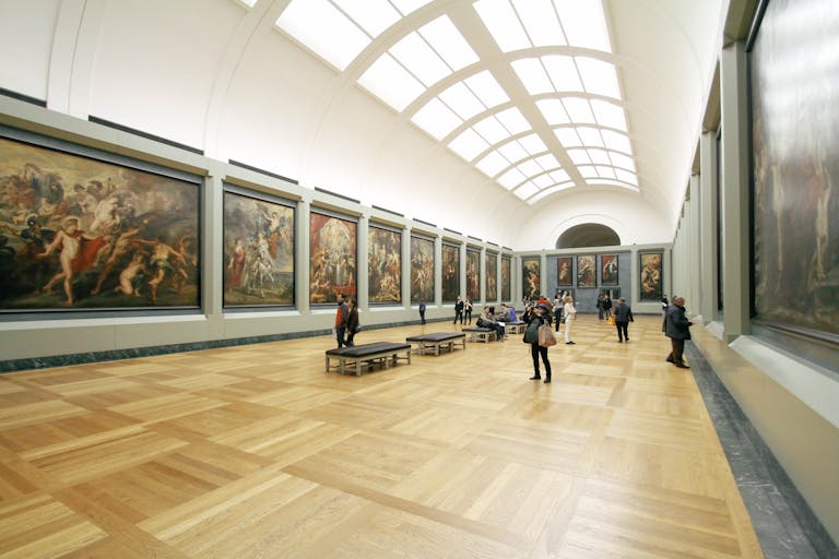 A wide view of a museum hall showcasing famous paintings and visitors exploring the art.