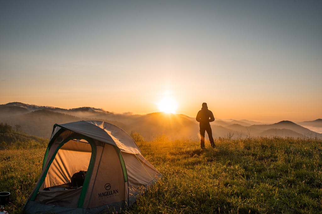 A camper enjoys the sunrise in a mountain setting with a tent. Perfect nature escape.