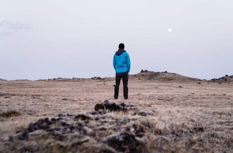 A lone hiker stands in a vast desert landscape under a full moon, capturing a sense of adventure and solitude.