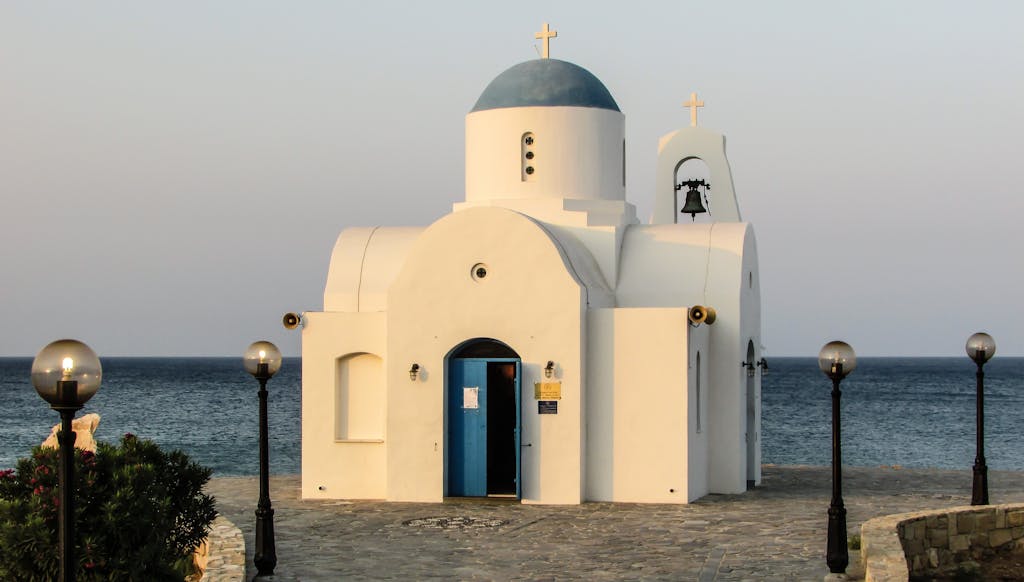 A traditional white chapel with blue dome and cross by the seashore, ideal for travel and architecture themes.