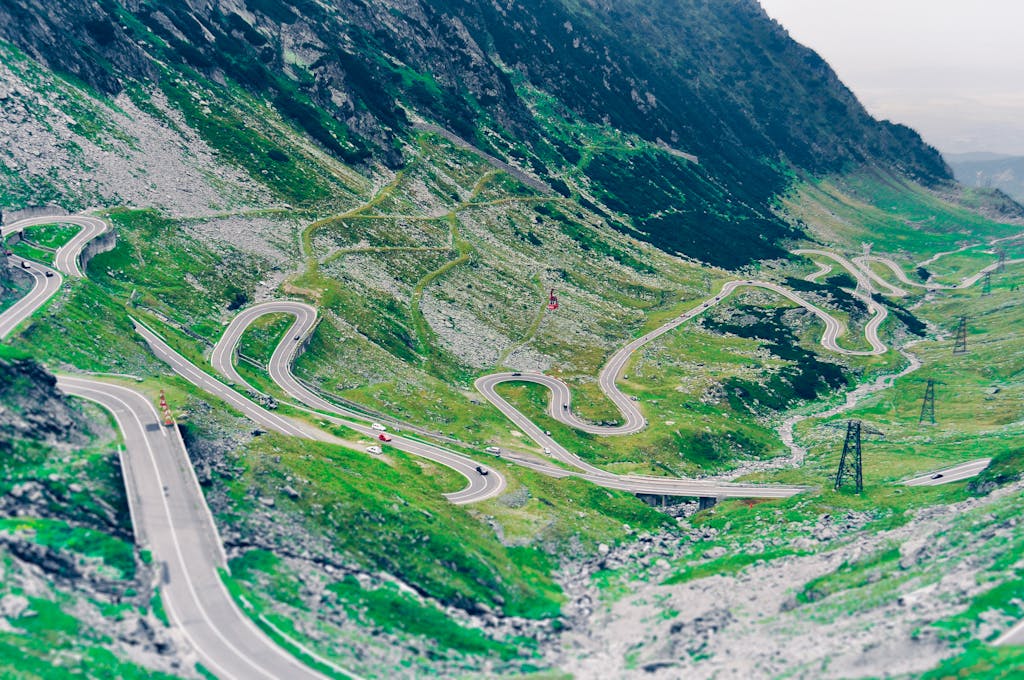 Aerial view of the winding Transfagarasan Highway in the Romanian mountains, showcasing lush greenery.