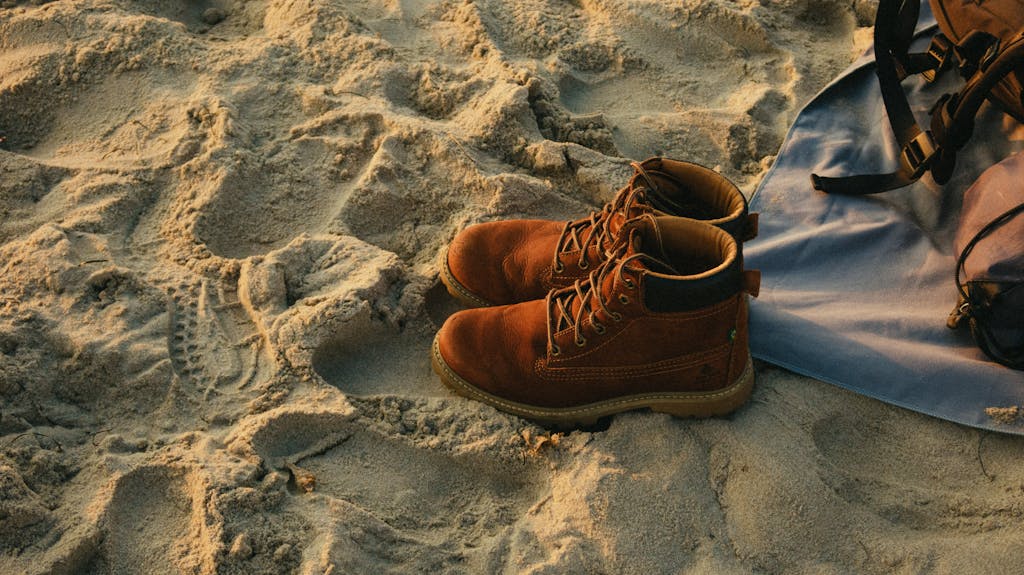 Brown leather boots on sandy beach background, ideal for travel themes.