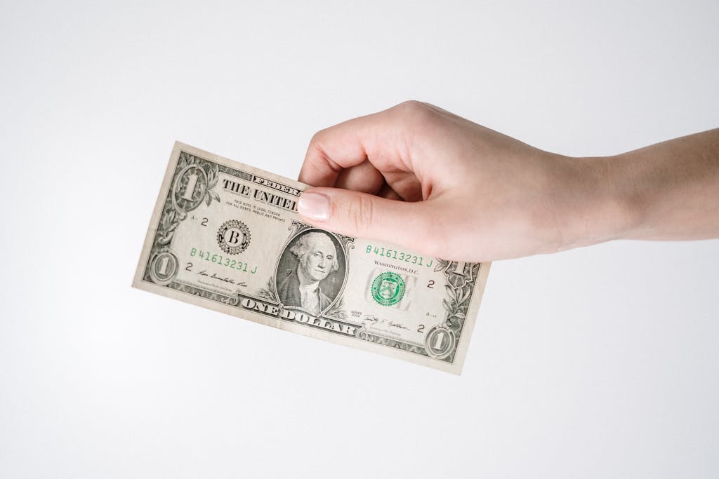 Close-up of a hand holding a one US dollar bill against a white background. Ideal for finance-related themes.