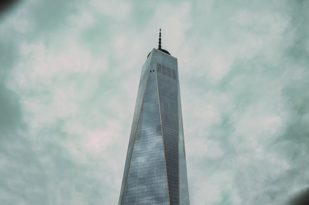 Dramatic view of One World Trade Center in New York City against overcast skies.