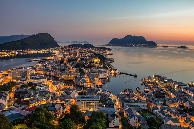 Explore the breathtaking skyline of Ålesund, Norway, illuminated against a stunning sunset over the harbor.