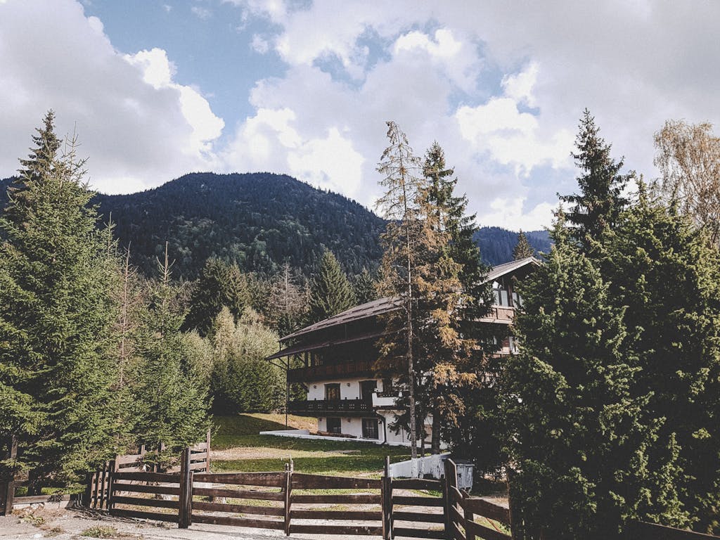 Idyllic cabin surrounded by lush forest and mountains under a vibrant sky.