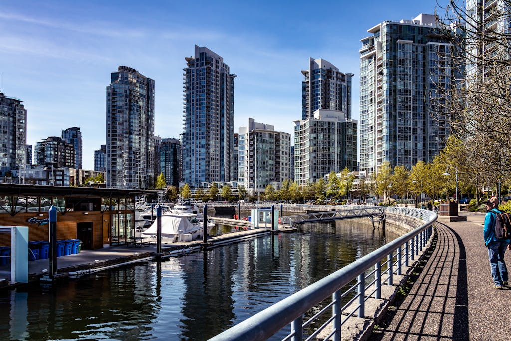 Modern skyscrapers reflect on the serene Vancouver waterfront in a bustling urban scene.