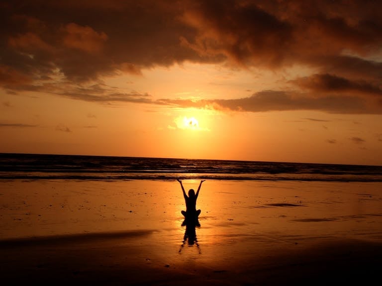 Peaceful meditation silhouette at sunset on a serene beach.