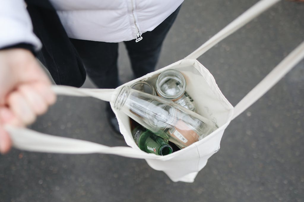 Person carrying a tote bag filled with glass bottles for recycling, promoting sustainability.