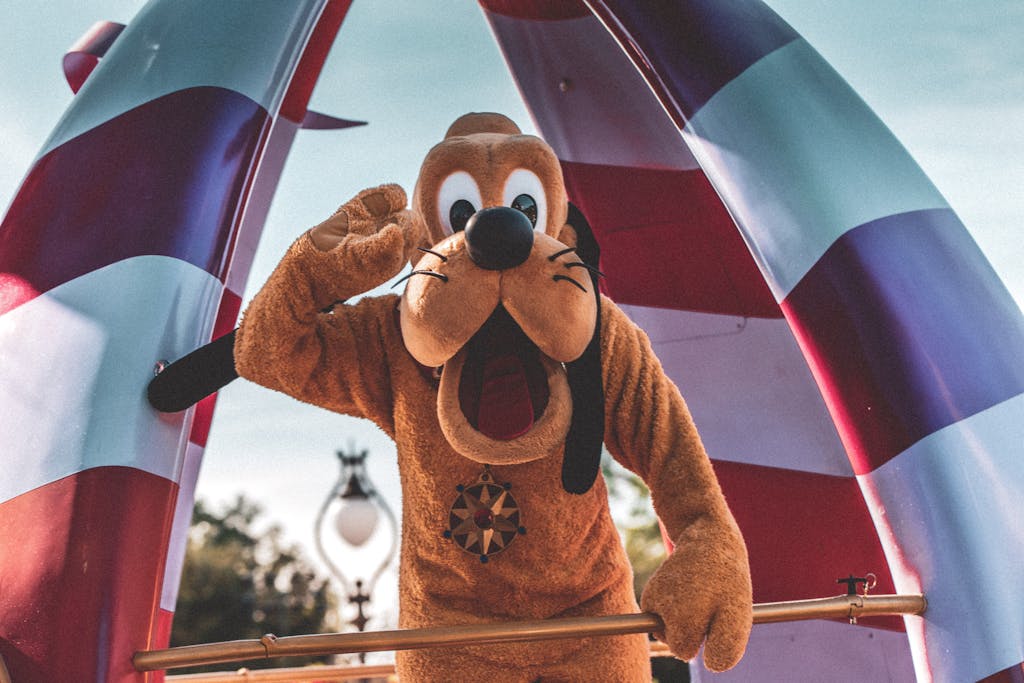 Playful Pluto character waving during a sunny Orlando parade at an amusement park.