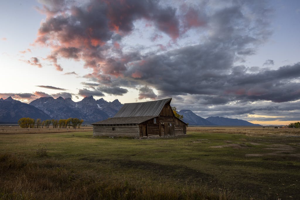 Scenic view of T A Moulton Barn with Tetons and vibrant sunset sky in Wyoming.