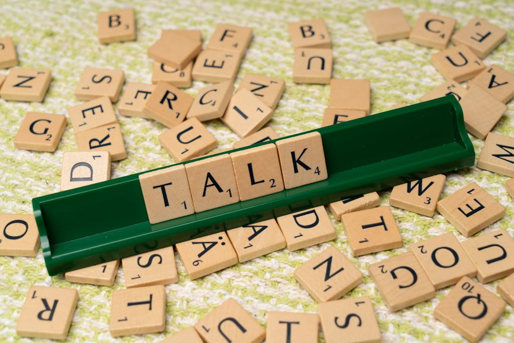 Scrabble tiles arranged to spell 'Talk' on a green tray, surrounded by scattered tiles on a textured surface.