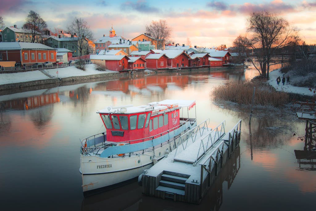 Snow-covered boats reflecting in Porvoo's historic harbor during a winter sunset.