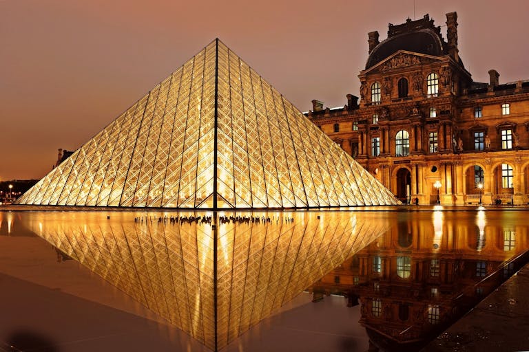 Stunning nighttime view of the illuminated Louvre Pyramid and reflection in Paris, France.