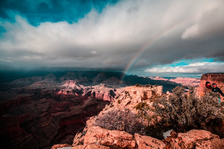 Stunning view of a rainbow arching over the Grand Canyon, capturing the majestic red rock formations under a dramatic sky.