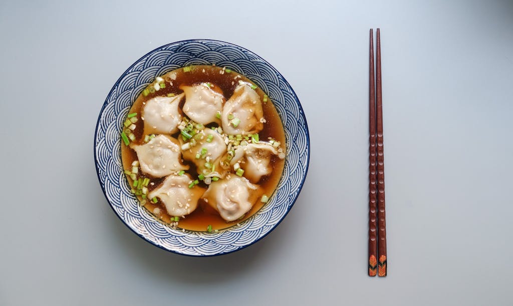 Top view of a bowl of dumplings in soup garnished with scallions.