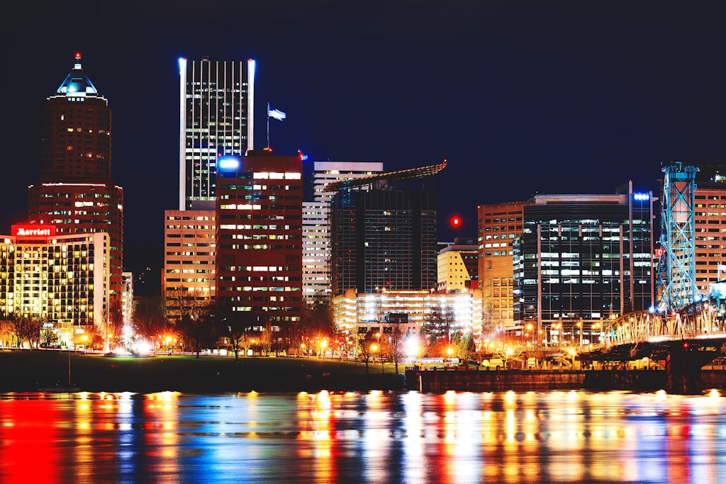 Vibrant Portland cityscape with reflections on the river and brightly lit skyscrapers at night.