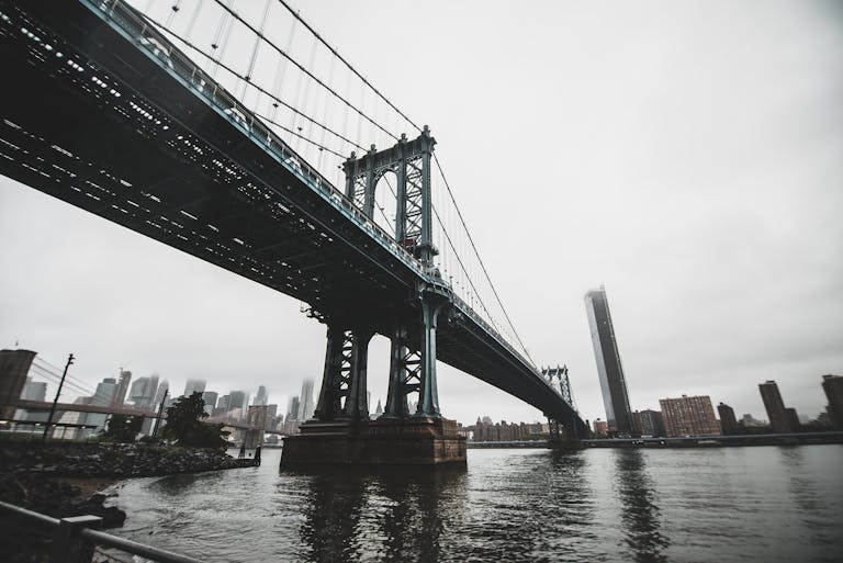 View of the Manhattan Bridge with New York City skyline in the backdrop on a cloudy day.