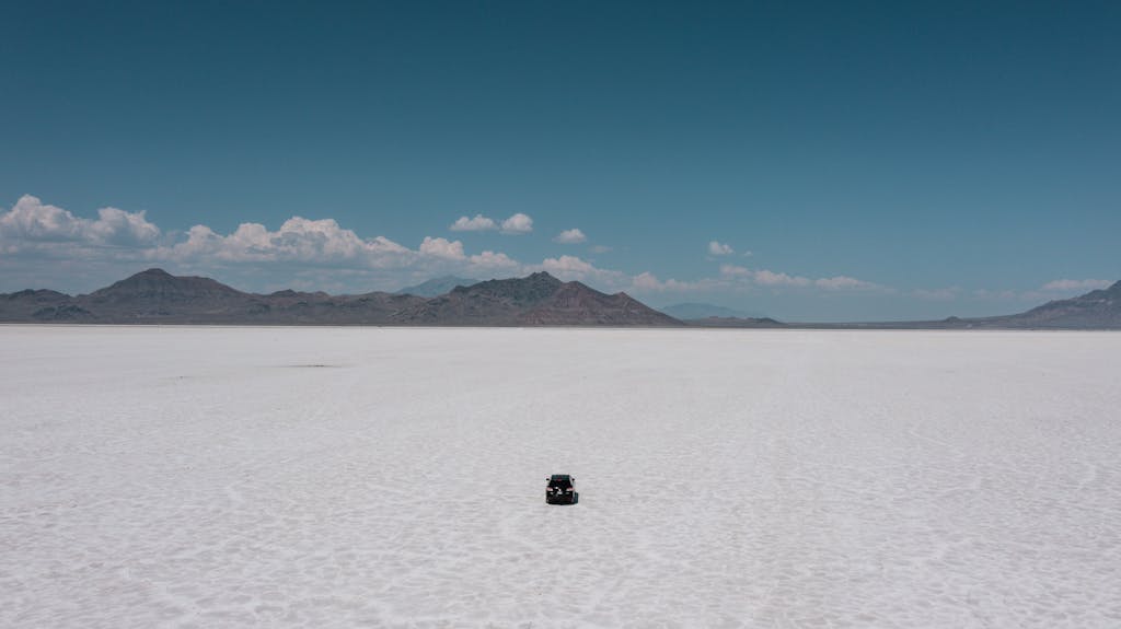 A solitary car navigating the expansive Bonneville Salt Flats under clear skies.