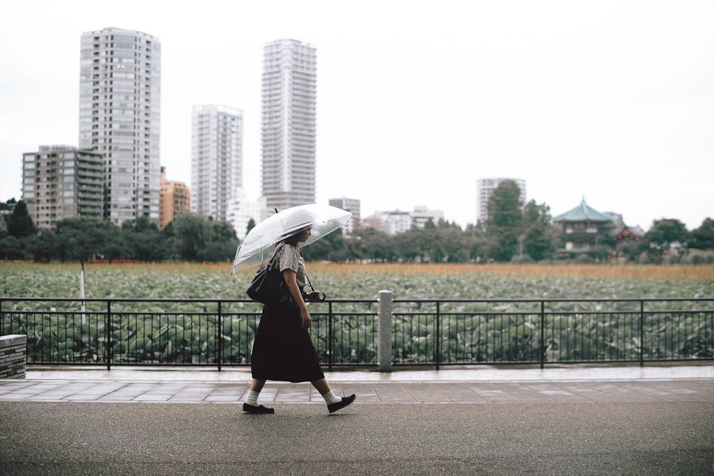 A woman with an umbrella strolls by a scenic city park in Tokyo, Japan.