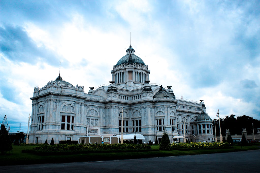 An ornate white palace with a dome under a dramatic cloudy sky in Thailand.