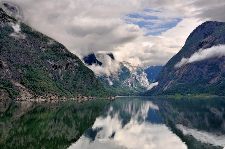 Breathtaking view of a Norwegian fjord with clear reflections and dramatic clouds.