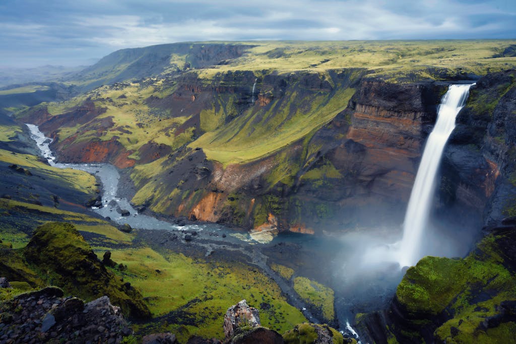 Breathtaking waterfall cascading into a verdant valley in Iceland's dramatic highlands.