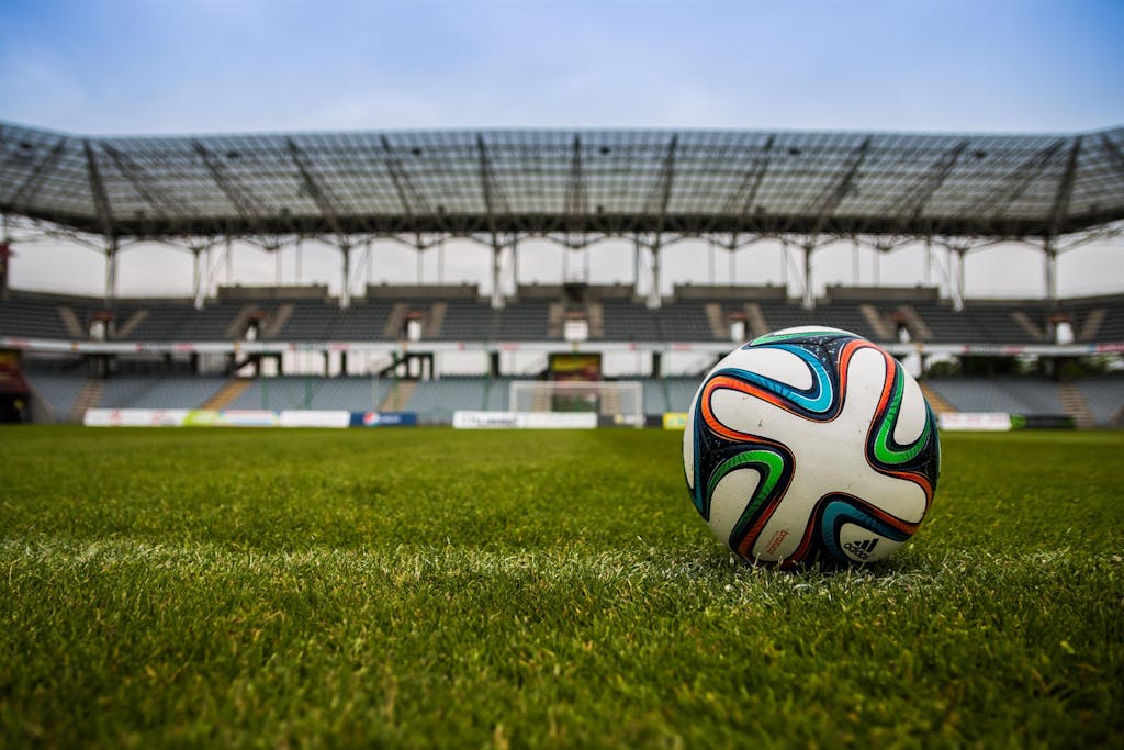 Close-up of a soccer ball on a lush grass field with an empty stadium in the background.