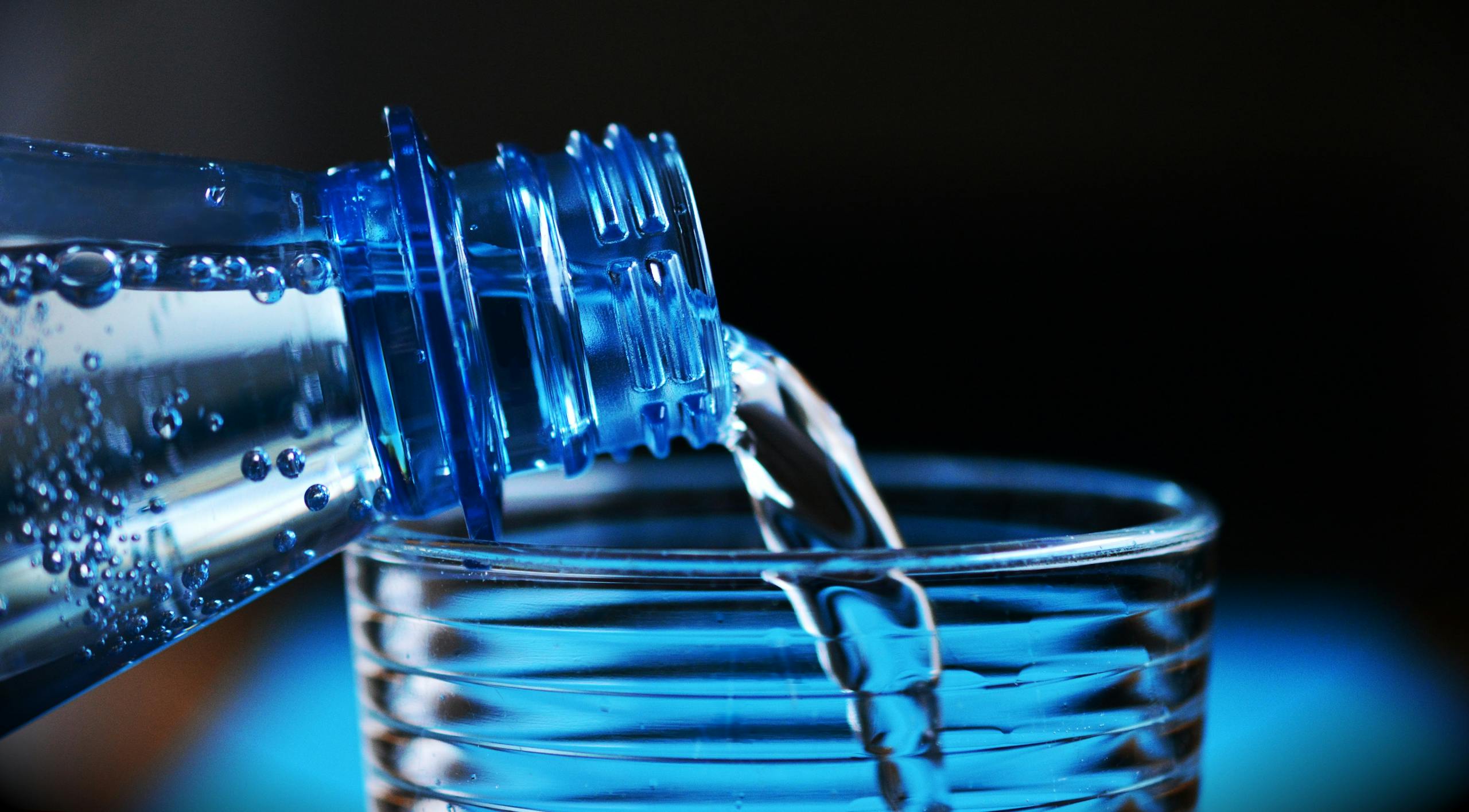 Close-up of sparkling water being poured from a bottle into a glass with bubbles visible.