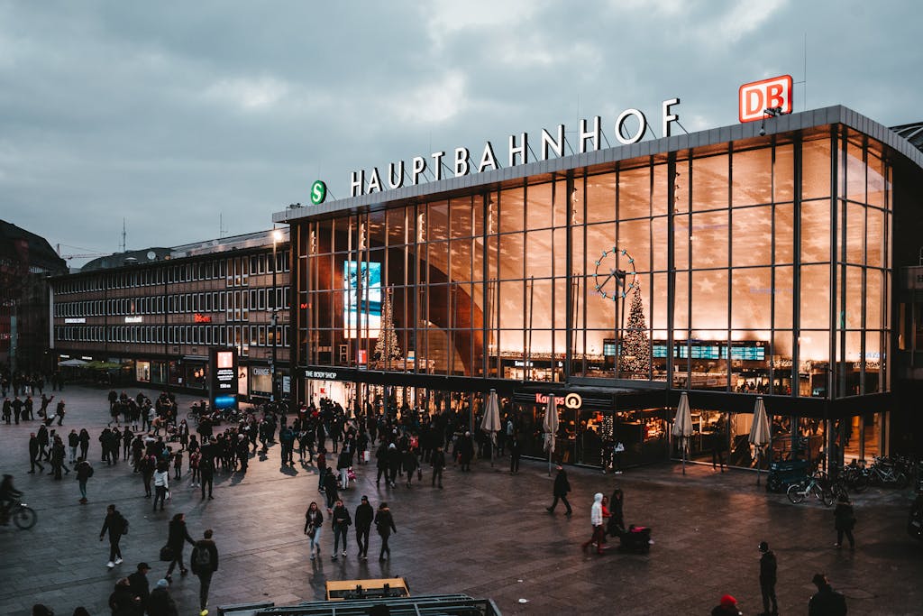 Crowd bustling in front of Cologne Hauptbahnhof during the evening, festive decor visible.