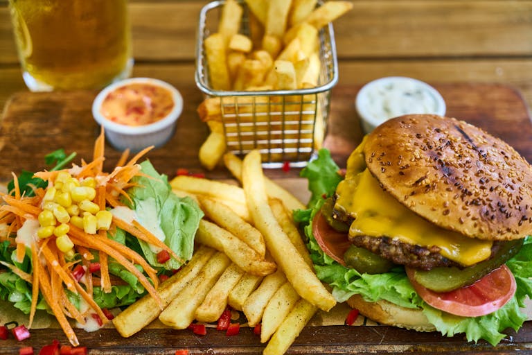 Delicious gourmet cheeseburger with crispy french fries and fresh salad on a wooden board.