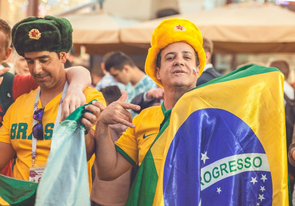 Enthusiastic Brazilian sports fans wearing colorful hats and holding flags at an outdoor gathering.