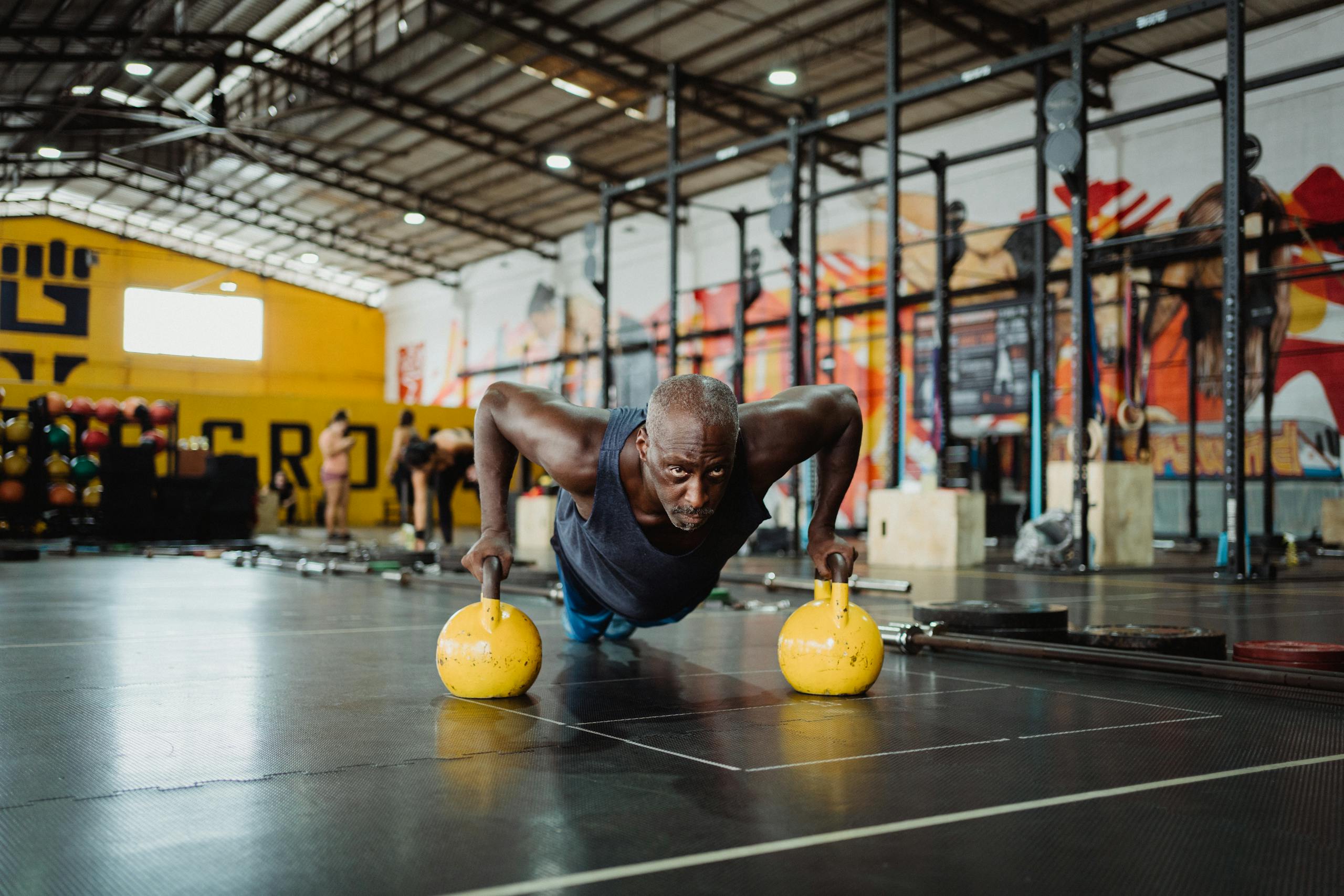 Focused man performing push-ups with kettlebells in a vibrant gym setting.