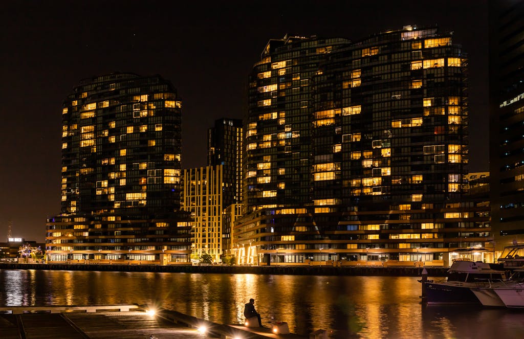 Illuminated modern buildings reflecting on water in Melbourne skyline during night.