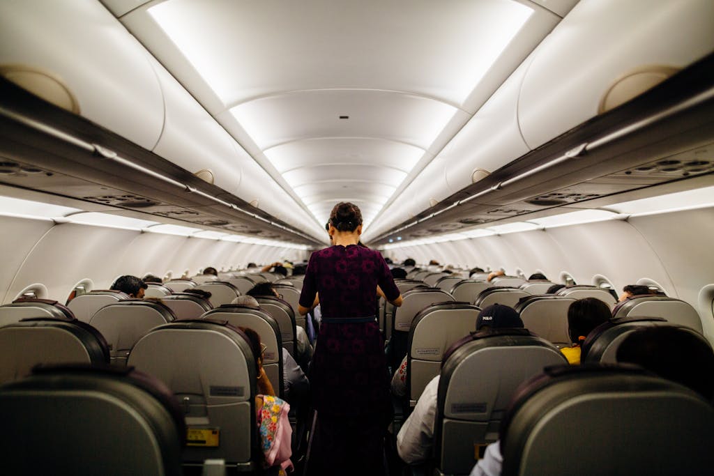 Interior view of an airplane cabin with passengers seated and a flight attendant walking down the aisle.