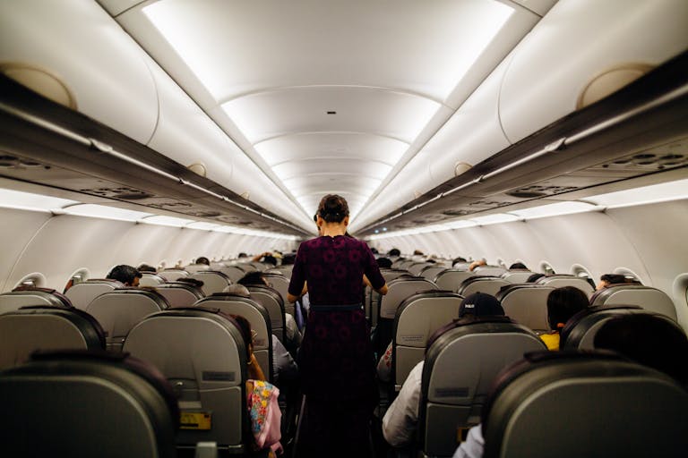 Interior view of an airplane cabin with passengers seated and a flight attendant walking down the aisle.