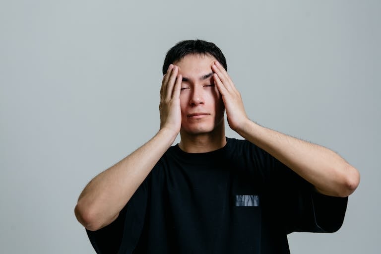 Man experiencing stress, hands on head, isolated on a gray background.