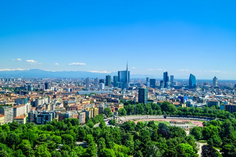 Panoramic view of Milan's skyline featuring modern skyscrapers and lush greenery under a clear blue sky.