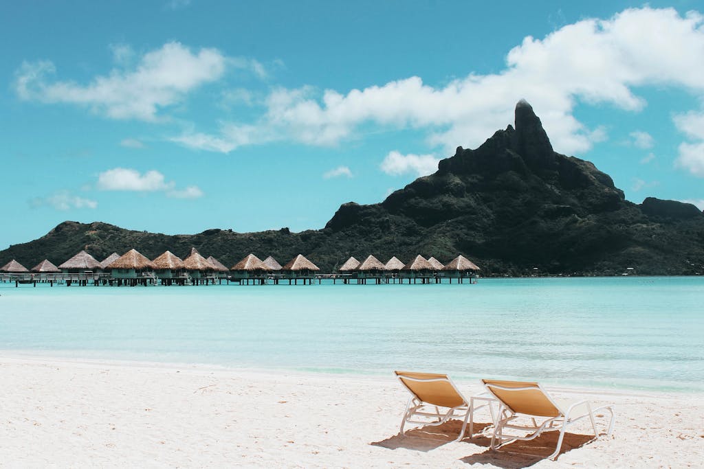 Pristine beach with loungers facing turquoise waters and iconic Mount Otemanu in French Polynesia.