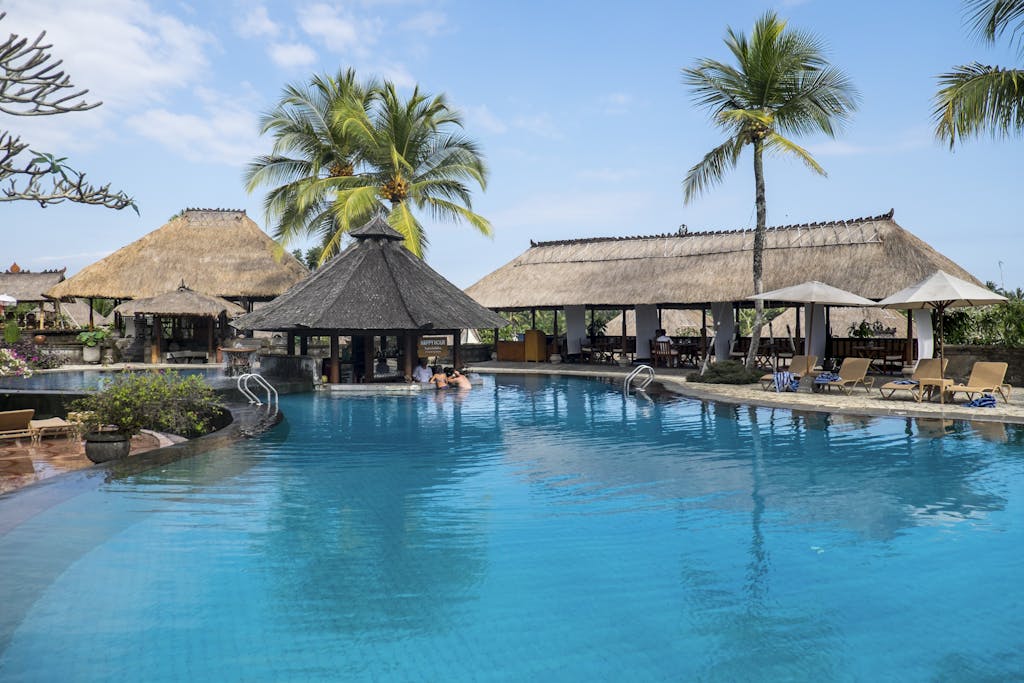 Relax by the tropical pool at a luxurious resort in Bali, featuring palm trees and serene blue waters.