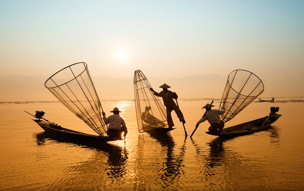 Silhouetted fishermen on Inle Lake, Myanmar casting nets in the golden sunrise.