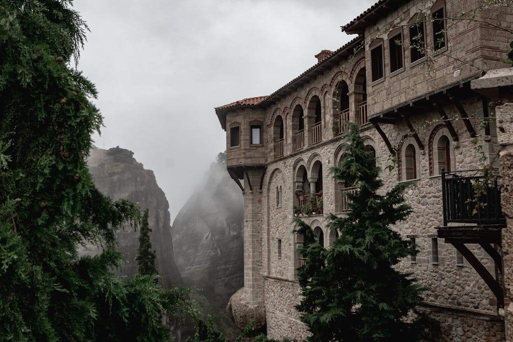 Stunning view of a historic Meteora monastery surrounded by fog and nature.