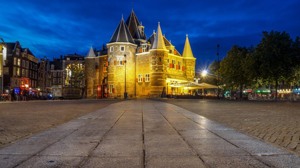 Stunning view of an illuminated medieval building in Amsterdam's city center during dusk.